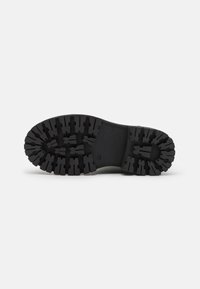 Semelle de chaussure en caoutchouc noir avec des motifs profonds, présentant un design robuste et un motif en relief pour une traction et une durabilité optimales.