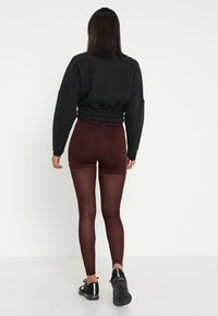 Sudadera negra recortada con dobladillo elástico, combinada con leggings burdeos de cintura alta que presentan una textura suave y brillante. Zapatillas de deporte negras.