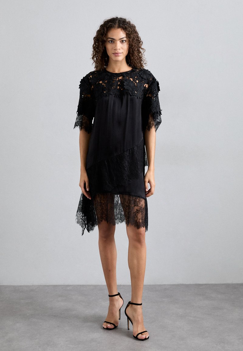 Μαύρο φόρεμα με λουλουδάτες δαντελωτές λεπτομέρειες, κο�ντά μανίκια, ασύμμετρο τελείωμα και άψητη δαντελένια επικάλυψη. Συνδυασμένο με μαύρα ψηλοτάκουνα σανδάλια.