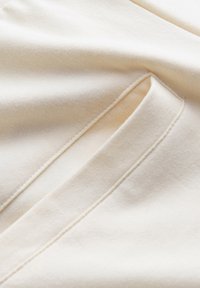 Lichtbeige stof met een zachte textuur, voorzien van een zijzak met nette stiksel en subtiele kreukels van het vouwen.