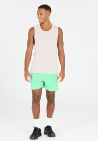 Lys beige ærmeløs tanktop med en lille grøn trykt detalje, parret med lys grøn badebukser, sorte sneakers og hvide sokker.