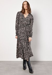 Schwarz und pink gemustertes langärmeliges Kleid mit V-Ausschnitt, elastischem Bund und gestuftem Rock. Kombiniert mit schwarzen Cowboy-Stiefeln.