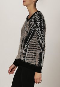 Maglione nero e grigio con una texture morbida, caratterizzato da motivi geometrici e un design a V. I polsini e l'orlo a coste completano il look.