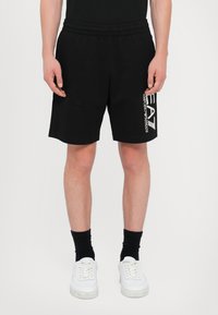 Black cotton shorts feature an elastic waistband and side logo print. Styled with black socks and white sneakers.