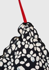 Svart tyg med ett pebbligt mönster i vitt och ljusblått, med en scalloped kant och ett rött handtag. Texturerad sömdetalj är synlig.