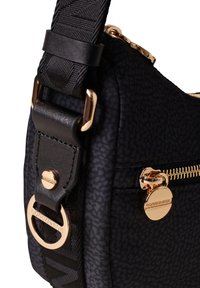 Borsa a mano in tessuto nero con hardware dorato, dotata di chiusura con zip e tracolla decorata. Superficie texture con un motivo sottile.