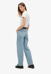 Jeans de denim azul claro con un corte relajado, que cuentan con dos bolsillos traseros, costuras en contraste y dobladillos deshilachados. Combinados con una camiseta blanca.