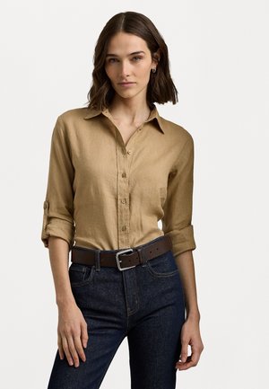 Ljusbrun skjorta med knappar och uppvikta ärmar, tillverkad av linne, i kombination med mörkblå jeans och ett mörkbrunt bälte med en silverfärgad spänne.