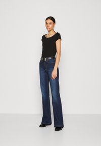 Top scurt negru cu mansete, asortat cu blugi din denim de culoare albastru închis, cu talie înaltă și flared. Cintură neagră cu accente argintii și cizme negre până la gleznă.
