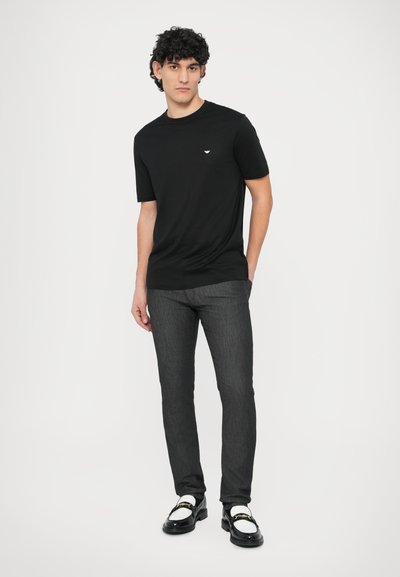 Juoda trumpomis rankovėmis marškinėliai su subtiliu logotipu, derinami su tamsiai pilkomis siaurėjančiomis džinsomis ir juodais batais su baltais akcentais.