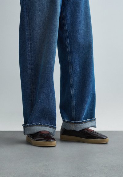 Crne lakirane tenisice s gumenim potplatima, s teksturiranim dizajnom i bordo naglascima, u kombinaciji s ležernim plavim trapericama.