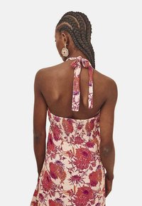 Vestido estilo halter con un estampado floral en rosa, rojo y púrpura. Presenta un corpiño fruncido y un lazo en el cuello. Textura de tela suave.