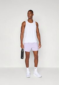 Valge varrukateta topp, helelilla lühikesed püksid, valged tossud ja käes hoitud must joogipudel. Lihtne sportlik disain, vabaaja lõige.