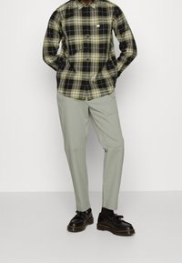 Plaid shirt with green, black, and white colors; light green trousers; black shoes with a textured surface and visible stitching details.