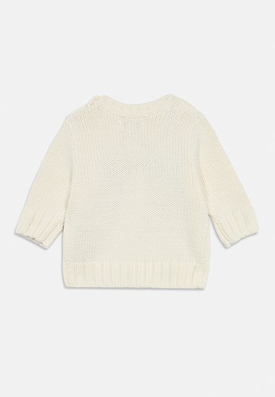 Stickad krämfärgad tröja med korta ärmar, ribbat nacke, muddar och nederkant. Har en lös vävstruktur och en sidoknappsdetalj på axeln.