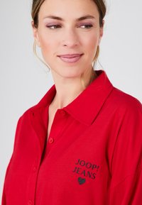 Červená košile na knoflíky s límcem, na levé straně s logem "JOOP! JEANS" a grafickým motivem srdce v černé barvě. Jemná tkanina.