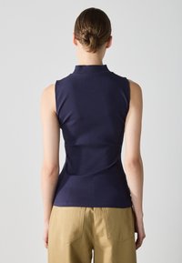 Top sin mangas de canalé en color navy con cuello alto, silueta ajustada y tejido texturizado; combinado con pantalones de talle alto en color beige.