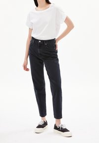 Jean noir taille haute avec une coupe droite, associé à un t-shirt blanc ample et des baskets noires avec une semelle blanche épaisse.