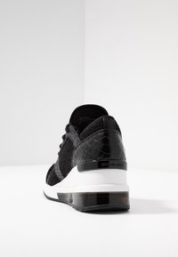 Sneaker nera con tessuto testurizzato e dettagli in stampa serpente. Presenta una suola intermedia bianca e una sezione del tallone trasparente. Lacci e marchio ben visibili.