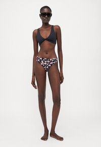 Svart bikini topp med tvist foran, sammen med svart bikini underdel med blomsterprint. Modell som har på seg svarte solbriller.