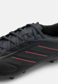 Black soccer cleat with textured synthetic material, featuring red accents, laces, and pronounced design lines on the side.