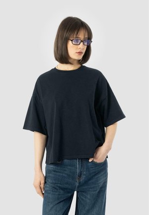 T-shirt nera oversize in cotone, con maniche corte, scollatura rotonda e vestibilità rilassata, abbinata a jeans in denim blu.