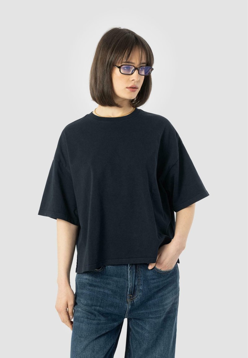 Sort oversized t-shirt i bomuld med korte ærmer, rund halsudskæring og en afslappet pasform, kombineret med blå denimjeans.