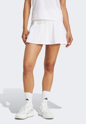 Falda atlética blanca con un diseño en capas, combinada con zapatillas blancas y calcetines con detalles en negro. Textura suave y tejido ligero.