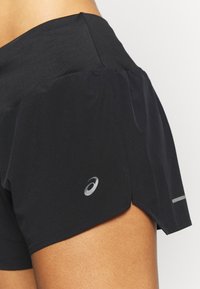 Svarta löpshorts med texturerad midja, lagerdesign, reflektionslogotyp och sidoklipp för flexibilitet och rörelse.