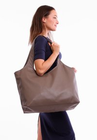 Large brown tote bag made of smooth synthetic material. Features wide straps and a minimalist design with a subtle embossed logo on the front.