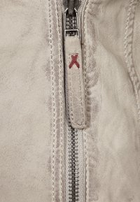 Grijze leren jasrits met zilveren tanden, voorzien van een stoffen trekband met rode stiksels en een gestructureerd oppervlak.