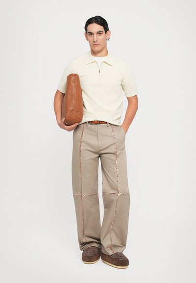 Beige gebreide polo met korte mouwen en rits, tan tas, brede taupe broek met roségouden stiksels, bruine instap schoenen met geborduurde details.