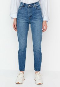 High-waisted blue denim jeans with a straight leg fit, featuring a classic five-pocket design and minimal fading, paired with white sneakers.