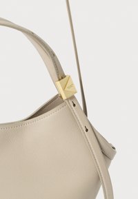 Beige læderhåndtaske med en blød tekstur, der har en struktureret krop, gyldent metalhardware og en justerbar skulderrem.