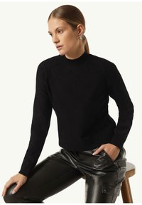 Schwarzer, gestrickter Pullover mit ribbeligem Rundhalsausschnitt und dezenten Verzierungen. Kombiniert mit glänzenden, schwarzen Lederhosen, die eine schlanke Passform zeigen.