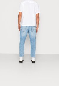 T-shirt bianca a maniche corte e jeans in denim azzurro chiaro. I jeans hanno una vestibilità dritta e due tasche posteriori. Le calzature sono bianche con suola nera.