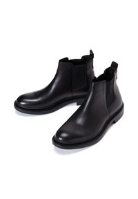 Stivaletti Chelsea in pelle nera con pannelli laterali elastici, punta tondeggiante e texture liscia. Presentano un tacco basso e una suola a contrasto.