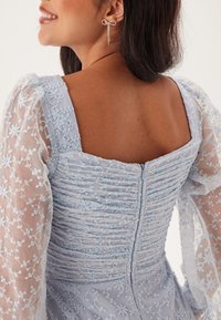 Světle modré šaty se strukturovaným korzetem, shromážděným zadním dílem a průhlednými, vyšitými balónovými rukávy. Obsahují květinové vzory a zipové zapínání.