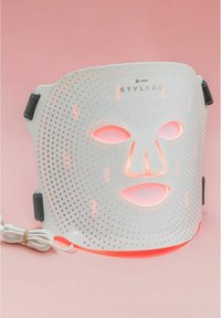 Masque facial LED blanc avec une surface perforée, accents de lumière rose, straps ajustables et un cordon d'alimentation connecté pour une utilisation.