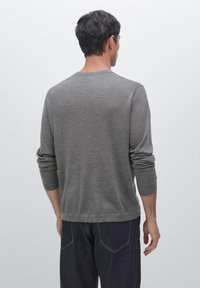 Maglione grigio a maniche lunghe realizzato in tessuto morbido, caratterizzato da un colletto rotondo e un design leggermente aderente. La vista posteriore mostra dettagli minimi.