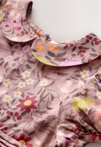 Vestido de tela floral con fondo marrón rosado, que presenta un cuello con volantes y elaborados patrones de flores en varios colores.