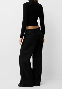 Jeans anchos negros de tiro alto, hechos de denim. Cuentan con bolsillos traseros y detalles de costura mínimos. Se llevan con una camiseta ajustada negra.