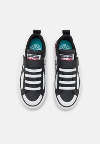Sneakers neri con lacci bianchi, suole in gomma e una cinghia in velcro. Presentano una toppa con logo rossa e bianca e solette turchesi.