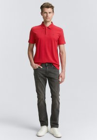 Rød polo-shirt med korte ærmer og krave, parret med grå jeans. Hvide sneakers fuldender outfitet. Stoffet ser glat og afslappet ud.