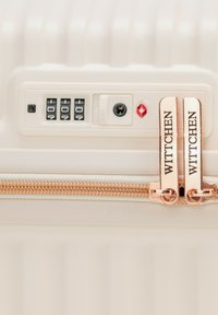 Biała walizka z twardą skorupą o teksturowanej powierzchni, zamkiem błyskawicznym w kolorze różowego złota, zamkiem szyfrowym i otworem na klucz zatwierdzonym przez TSA dla bezpieczeństwa.