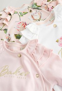 Tre body per neonati in rosa tenue, bianco e rosa floreale con spalle arricciate e bottoni a pressione dorati, disposti sovrapposti su una superficie piana.