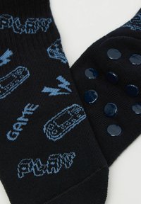 Czarne skarpetki z niebieskimi graficznymi wzorami przedstawiającymi kontrolery gier i błyskawice, z teksturowanymi niebieskimi gumowymi kropkami na podeszwach.