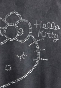 Grå stof med et Hello Kitty design lavet af klare rhinsten, der fremhæver karakterens ansigt og navn i dekorativ skrift.