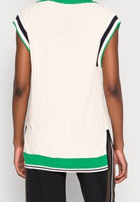 Haut en maille côtelée couleur crème avec un col vert, des manches courtes et des fentes latérales ; présente des accents rayés noirs et blancs à l'ourlet.