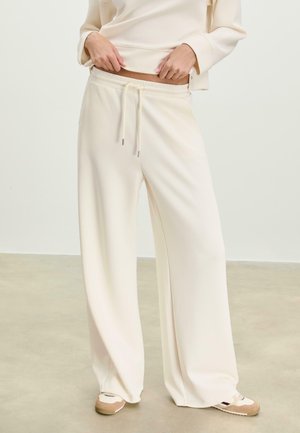Cream wide-leg pants with a smooth texture, elastic waistband, and drawstring. Paired with light-colored casual shoes.